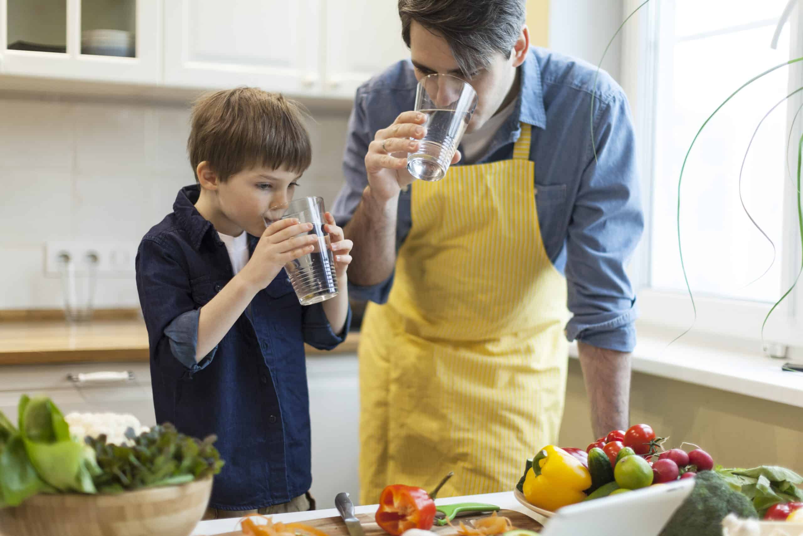 Father and son cooking healthy food in the kitchen and drinking water