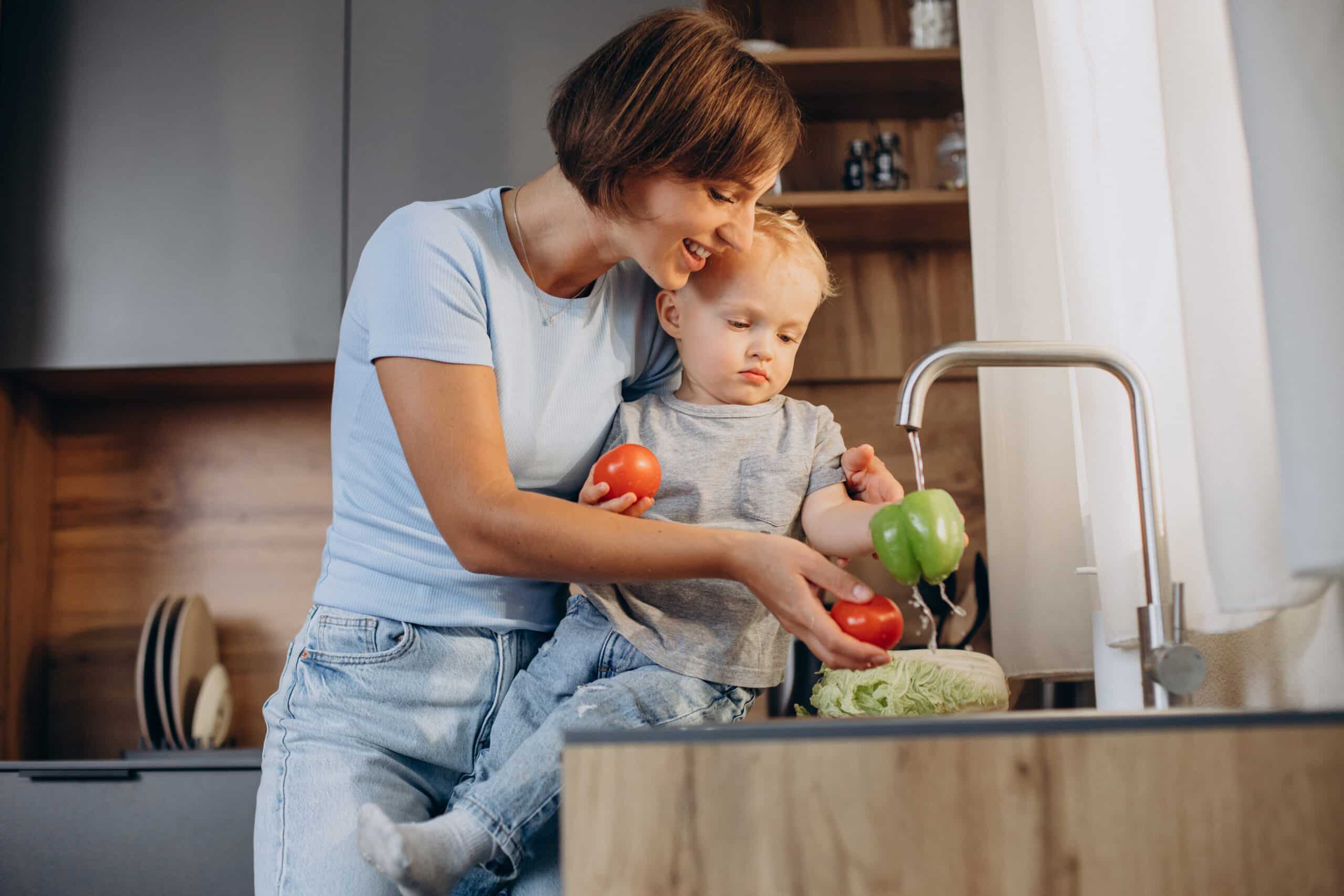 Woman with her son washing vegetables in the kitchen sink