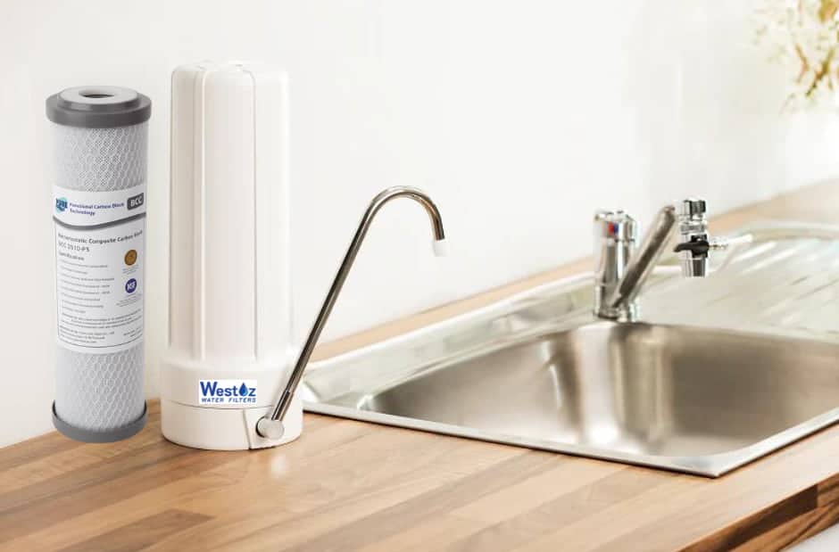 Westoz Water Filters benchtop water filter system installed on a kitchen counter next to a stainless steel sink, shown with a replacement carbon block filter cartridge