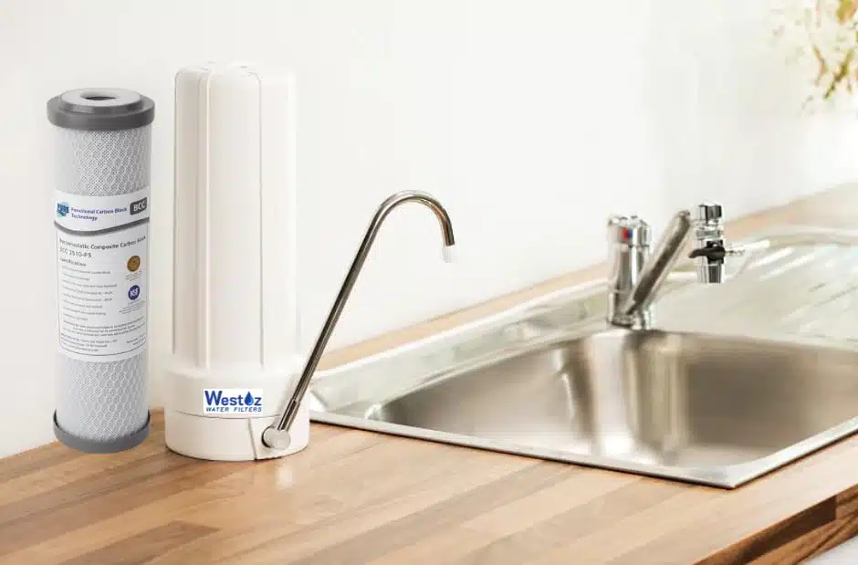 Westoz Water Filters benchtop water filter system installed on a kitchen counter next to a stainless steel sink, shown with a replacement carbon block filter cartridge